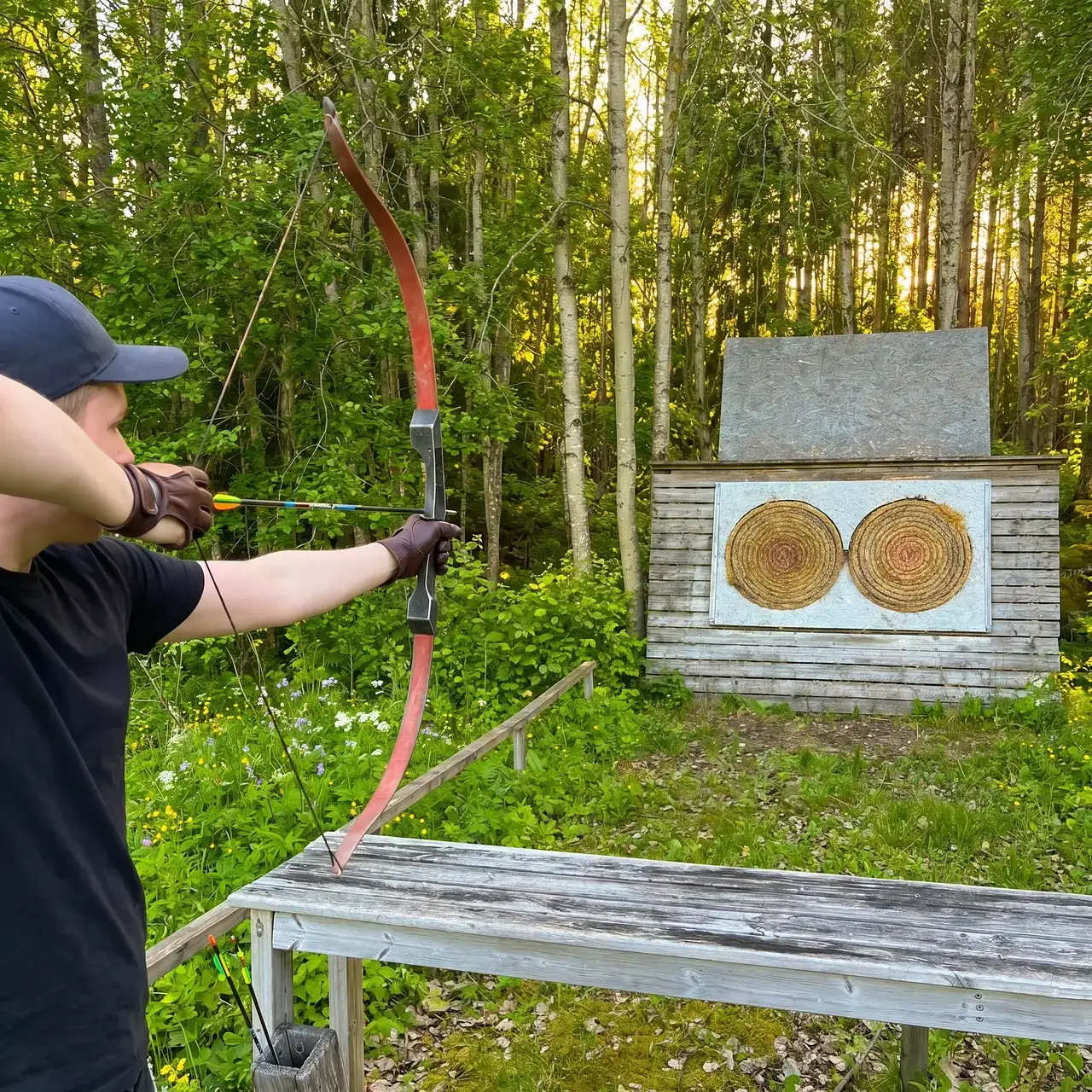 Person skjuter med pilbåge mot mål med två cirklar i skogen.
