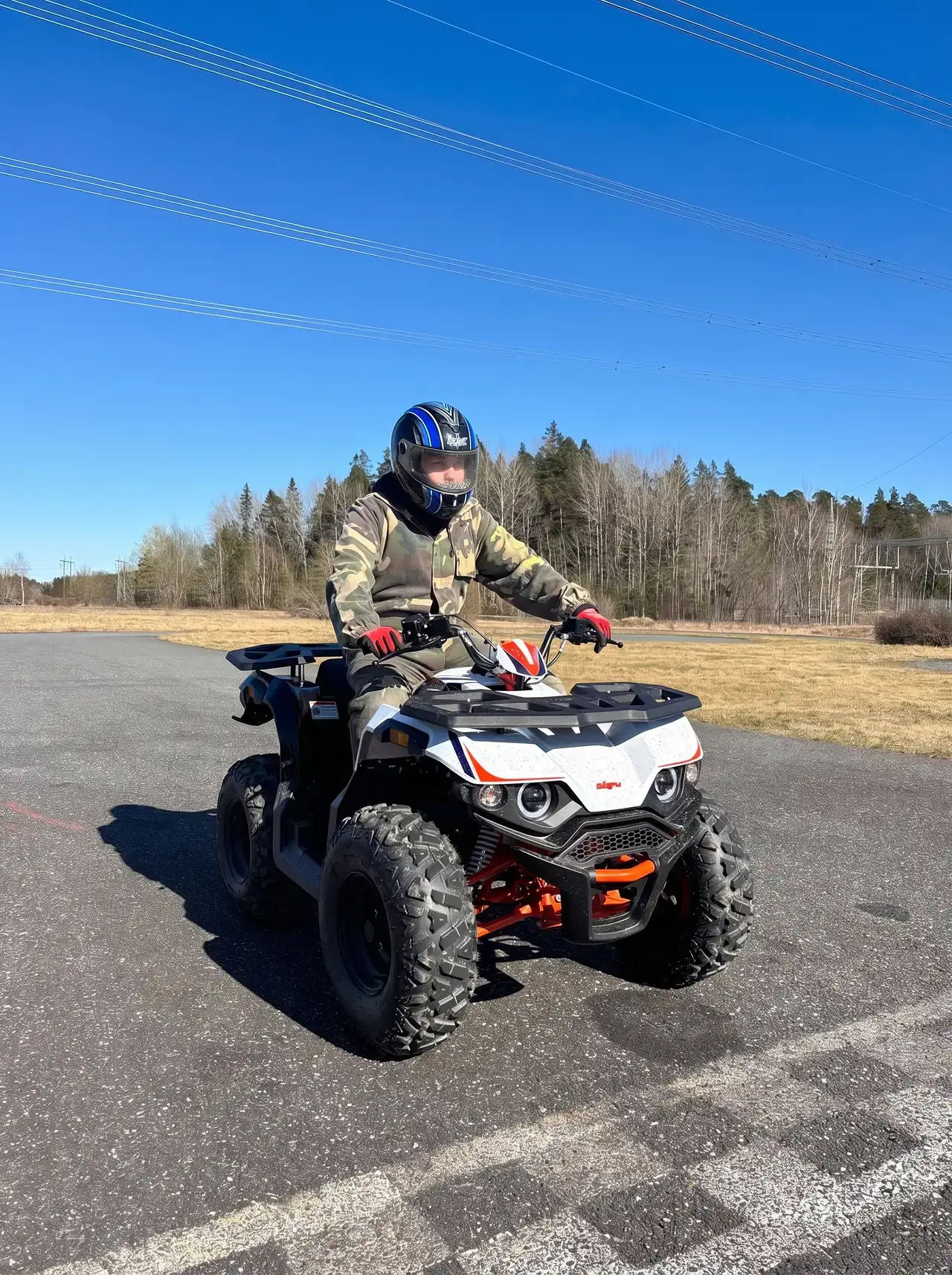 Person i hjälm kör fyrhjuling på asfalterad väg vid skogskant.