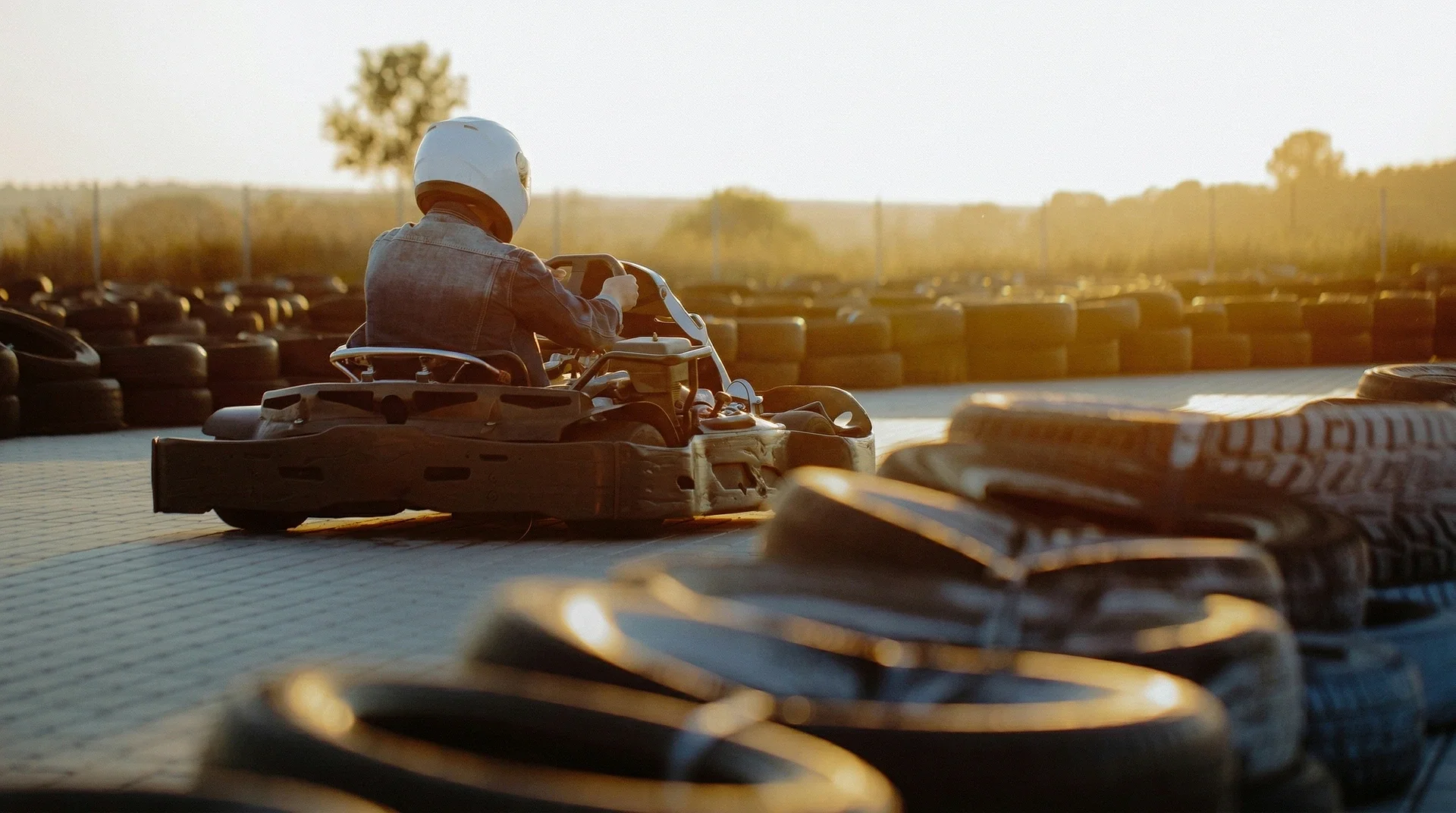 Person kör gokart på utomhusbana med däckbarriärer vid solnedgång.